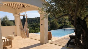A covered outdoor area with a hammock, a wooden chair, and a view of a swimming pool. - Atmospheric villa with nice sea view in a quiet green area (La Croix-Valmer)