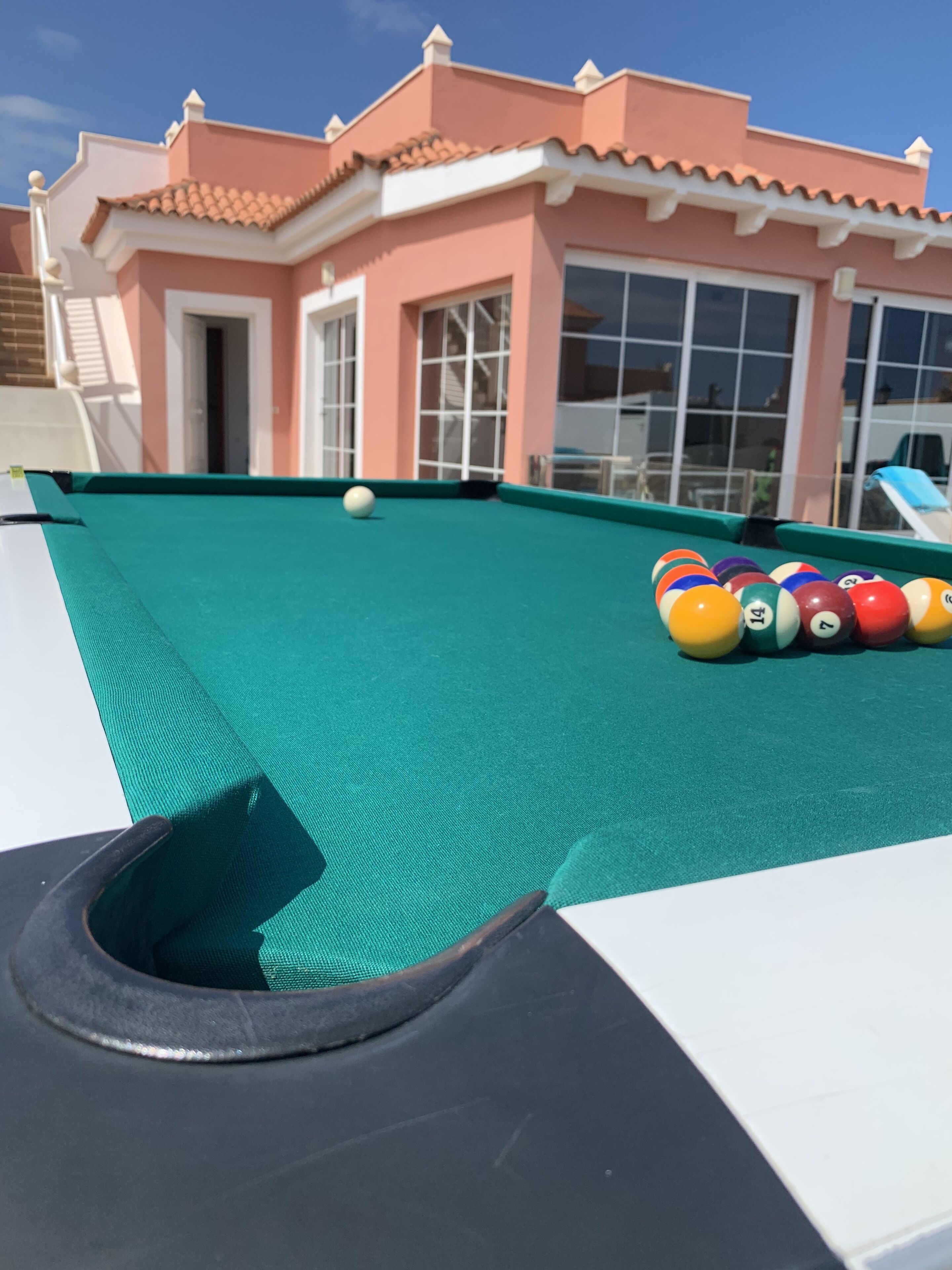 A pool table with balls and a house in the background.