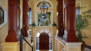 Un amplio pasillo con una escalera central, columnas ornamentales y un gran arco.