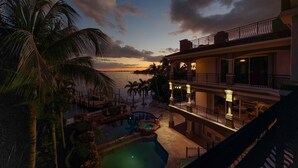 Un resort con piscina, palmeras y vistas al océano al atardecer.