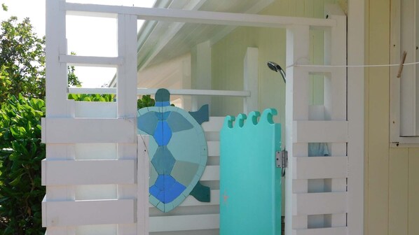 A white gate with a blue and green decorative panel, leading to a covered outdoor area with a shower.