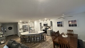 A modern kitchen with white cabinets, a central island, and a dining area with a wooden table and chairs. - OLD HOMESTEAD #1- STUNNING LAKE VIEWS! STEPS FROM LAKE ERIE! (Huron)