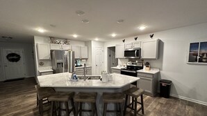 A modern kitchen with white cabinetry, a central island with bar stools, stainless steel appliances, and a herringbone wood floor. - OLD HOMESTEAD #1- STUNNING LAKE VIEWS! STEPS FROM LAKE ERIE! (Huron)