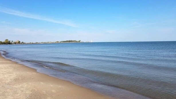 A beach with clear blue water and a distant lighthouse. - OLD HOMESTEAD #1- STUNNING LAKE VIEWS! STEPS FROM LAKE ERIE! (Huron)