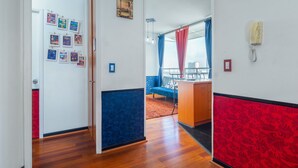 A hallway with a wooden floor, a red and blue patterned wall, a blue sofa, a wooden desk, and a telephone. - Best Location in Santiago, Chile! Great View & Full Equiped Apartment! (Santiago)