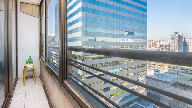 A balcony with a view of a cityscape, a hanging light fixture, and a small table with a green bottle and a white container. - Best Location in Santiago, Chile! Great View & Full Equiped Apartment! (Santiago)