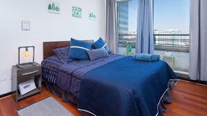A modern bedroom with a large bed, a nightstand with a lamp, and a view of the city through a large window. - Best Location in Santiago, Chile! Great View & Full Equiped Apartment! (Santiago)