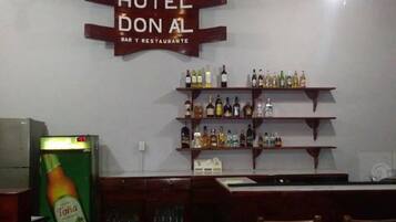 A bar area with a sign reading "HOTEL DON AL BAR Y RESTAURANTE" and shelves stocked with various bottles.