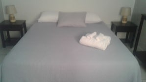 Una cama con cubrecolcha gris, una toalla blanca doblada y dos mesitas de noche con lámparas.