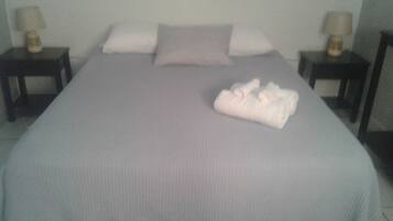 A bed with a grey bedspread, a folded white towel, and two bedside tables with lamps.
