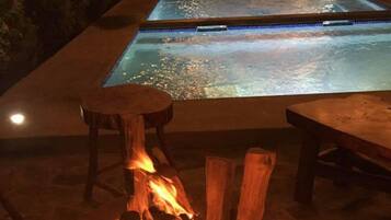 A pool area with a fire pit in the foreground and a pool in the background.