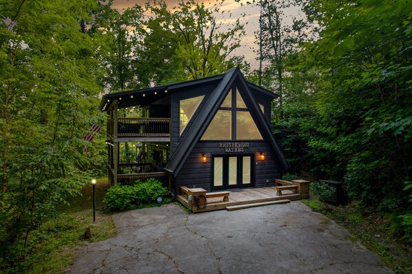 A wooden cabin with a balcony, a wooden deck, and a sign reading 'WHISPERING WATERS.'