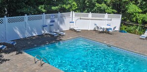 Una piscina rettangolare con acqua cristallina, circondata da un recinto bianco e ombreggiata da alberi.