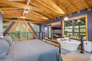 A bedroom with a large bed, a bathtub, and a view of the outdoors.