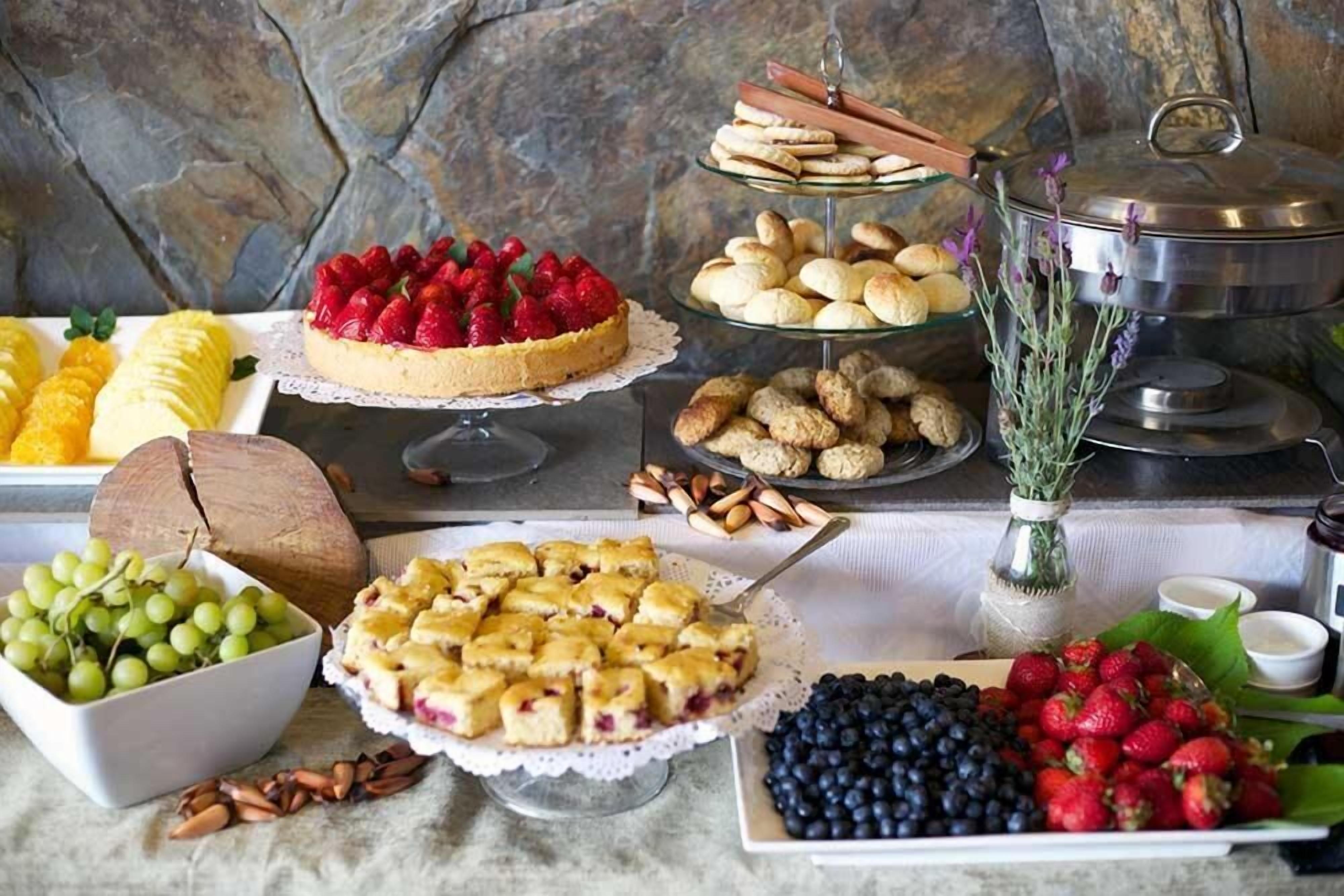 En buffet med forskellige spiser, herunder en frugttærte, kager og et udvalg af frugter som druer og jordbær.