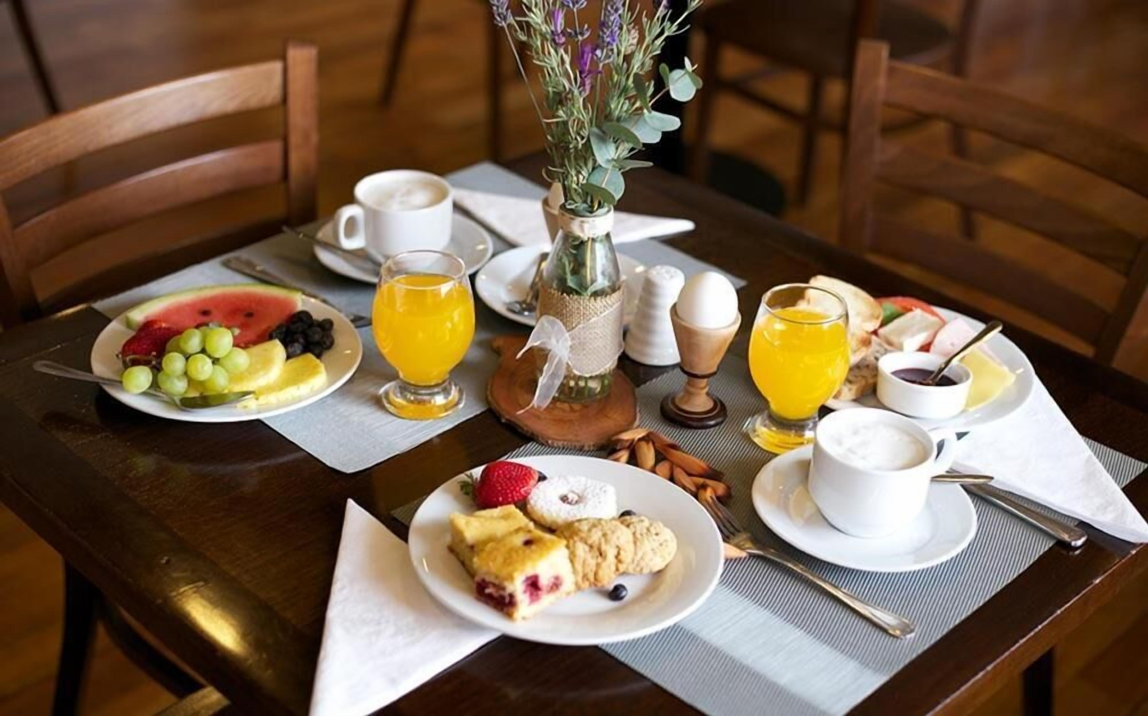 A breakfast setting with plates of fruit, pastries, and beverages on a wooden table.