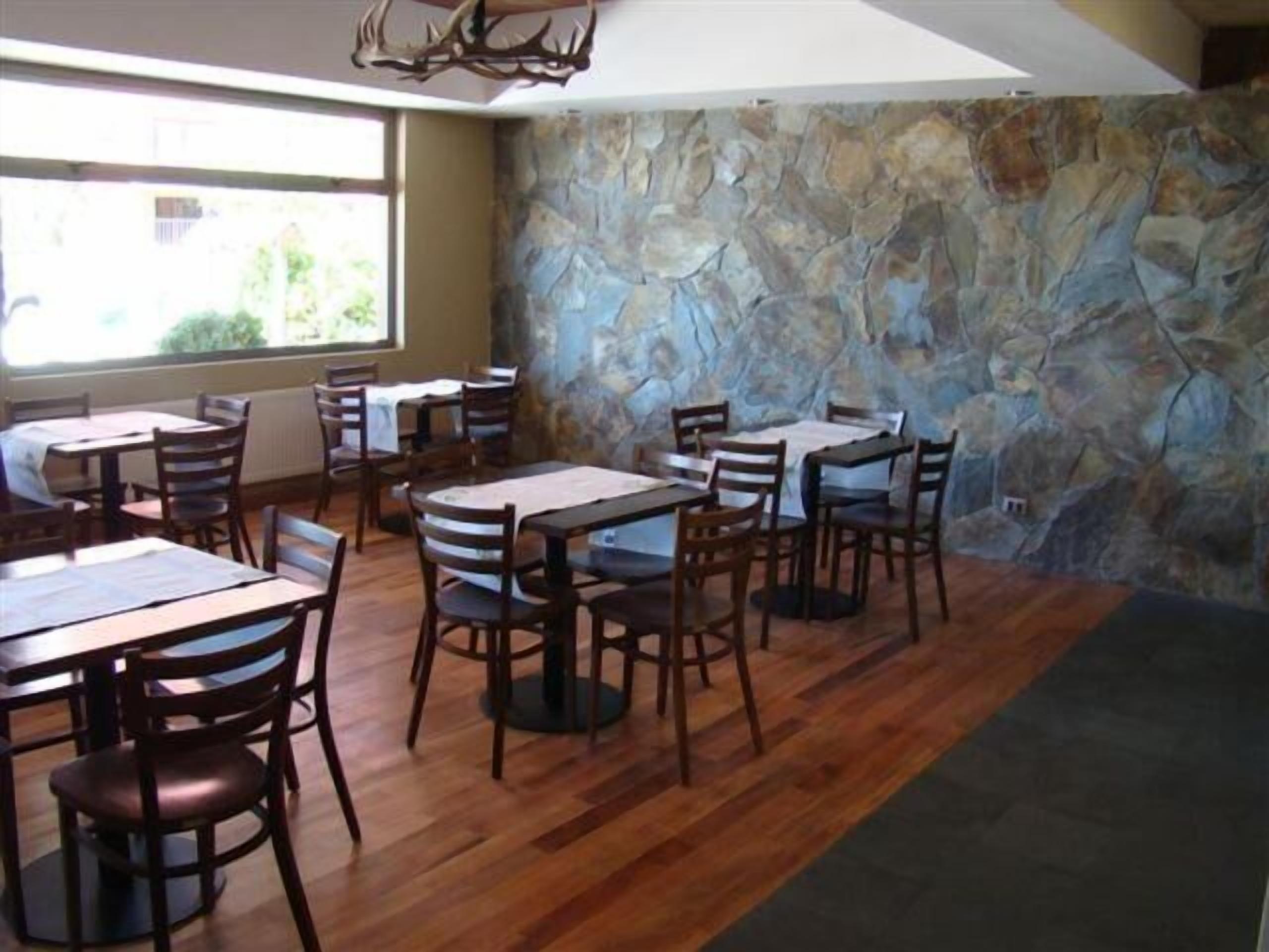 A restaurant with wooden tables and chairs, stone walls, and large windows.