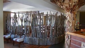Un área de recepción con un mostrador de madera, una zona de estar con sillas y un banco, y una pared con listones de madera verticales.