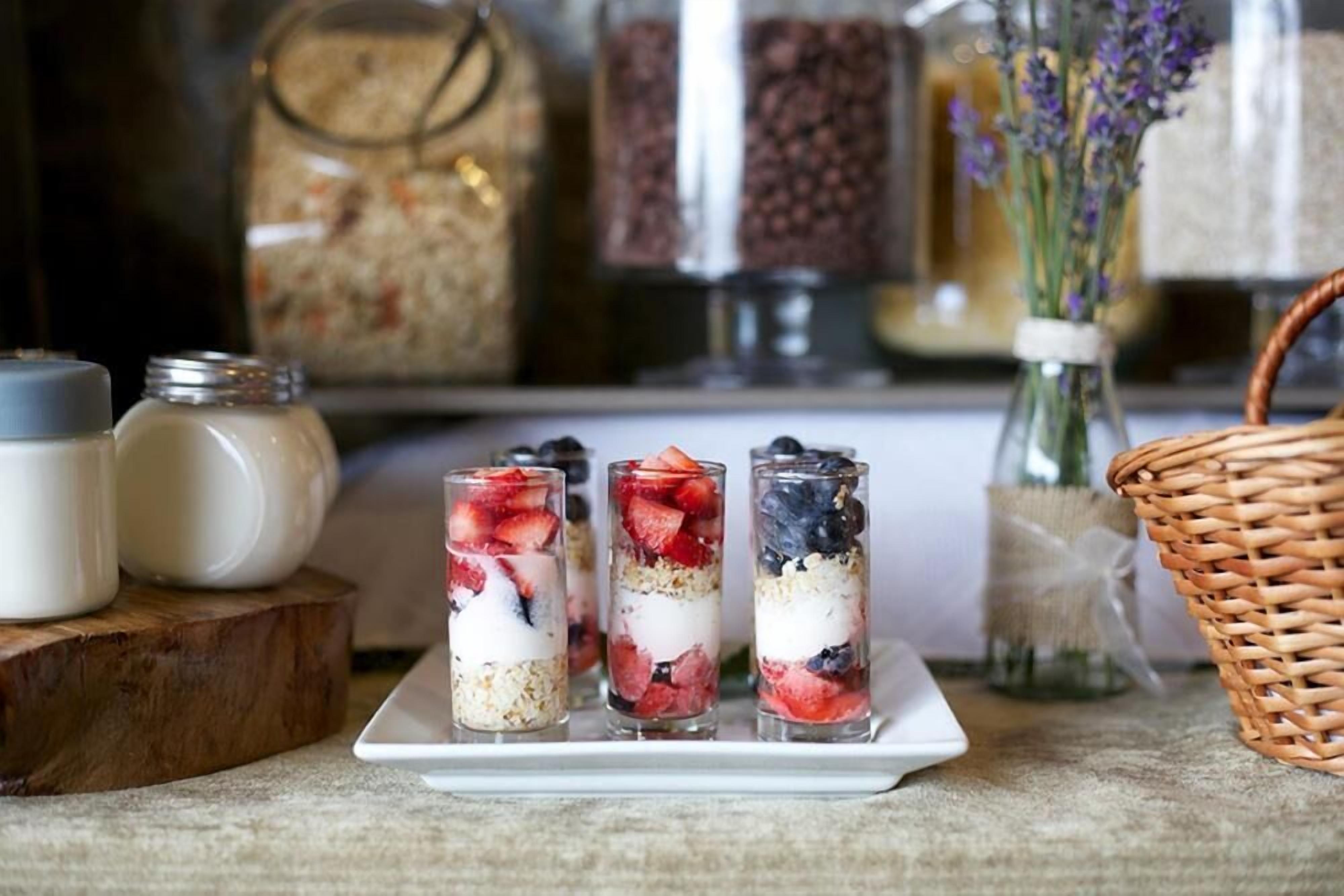 Tres vasos de parfait con capas de yogur, granola y frutos rojos sobre un plato blanco.