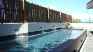 Una piscina rectangular con una cubierta de madera en primer plano y una valla de bambú al fondo.