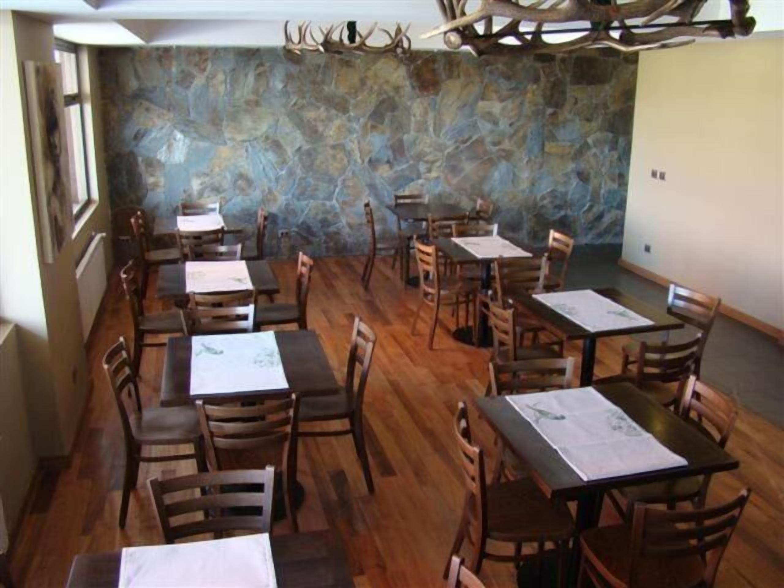Een eetgedeelte met houten tafels en stoelen, een stenen muur en een plafond met decoraties van gewei.