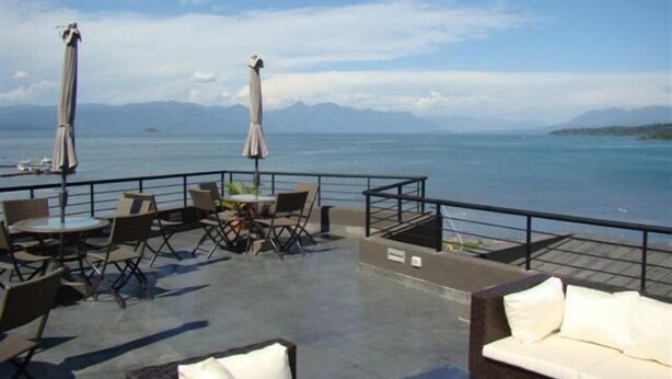 Un espacio al aire libre con mesas y sillas, sombrillas y vistas al mar y las montañas.
