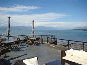 An outdoor seating area with tables and chairs, umbrellas, and a view of the sea and mountains. - Hotel Terraza Suite (Villarrica)