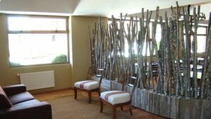 Una sala de estar con un sofá marrón, dos sillas de madera, un tapete tejido y una pared decorada con ramas verticales.