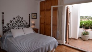 A bedroom with a bed, a wooden wardrobe, a door leading to a balcony, and a small table with a lamp. - Voramar CostaBravaSi - Pool, BBQ, views, wifi (S'Agaró)