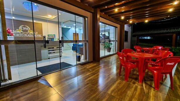 A modern hotel lobby with glass doors, wooden flooring, and red plastic chairs. - Conforto Plaza Hotel (Capitão Leônidas Marques)
