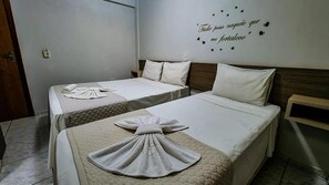 Ein Hotelzimmer mit zwei Betten, jeweils mit einem ordentlich gefalteten Handtuch und einem dekorativen Kissen. An der Wand ist eine Dekoration mit Herzen und Text zu sehen.