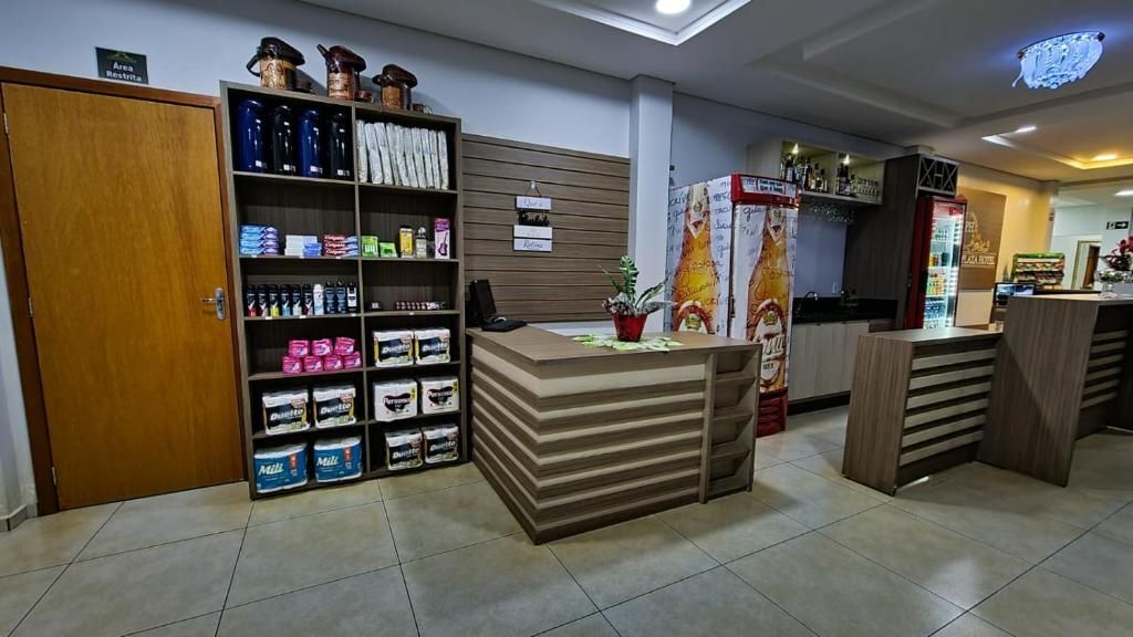 Un área de recepción con mostrador, estantes llenos de productos y una puerta con la leyenda 'Area Restrita'.