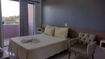 A hotel room with a bed, a chair, a bedside table, and a window with curtains.