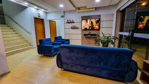 A hotel lobby with a staircase, blue sofas, a TV, and a reception desk. - Conforto Plaza Hotel (Capitão Leônidas Marques)