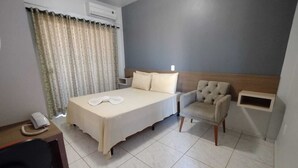 A hotel room with a bed, a chair, a desk with a phone, and a curtain. - Conforto Plaza Hotel (Capitão Leônidas Marques)