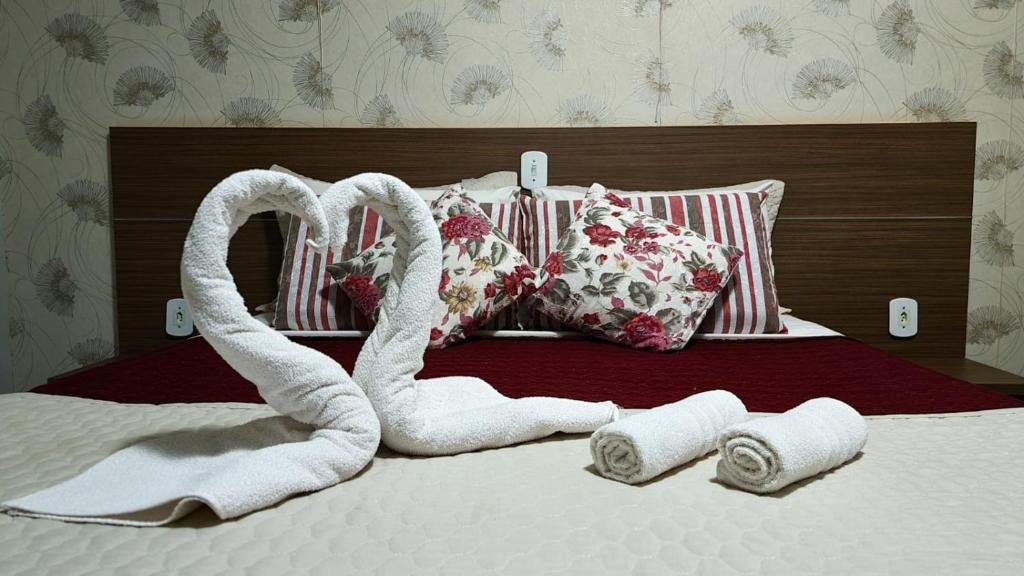 Una cama con una toalla dispuesta en forma de corazón, almohadas florales y una colcha roja.