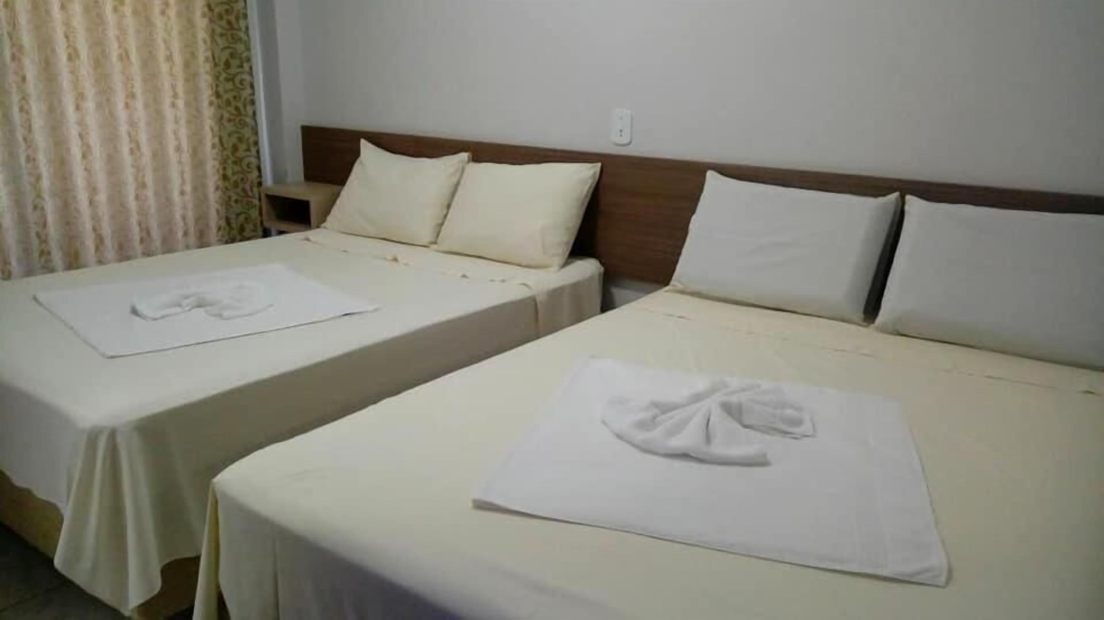 Two single beds with white linens and pillows, a wooden headboard, and a plain wall with a power outlet.