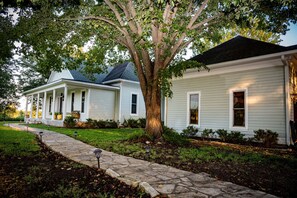 A row of two-story houses with a stone pathway leading to the front door, surrounded by well-maintained lawns and a large tree. - Chateau Relaxo - Farmhouse on 19 acres, Pool + pool house + Games, Sleeps 20 (Chappell Hill)