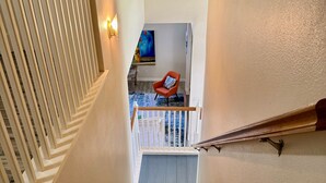 A staircase with dark wooden steps and white railings, leading to a landing with a blue rug and a red chair.