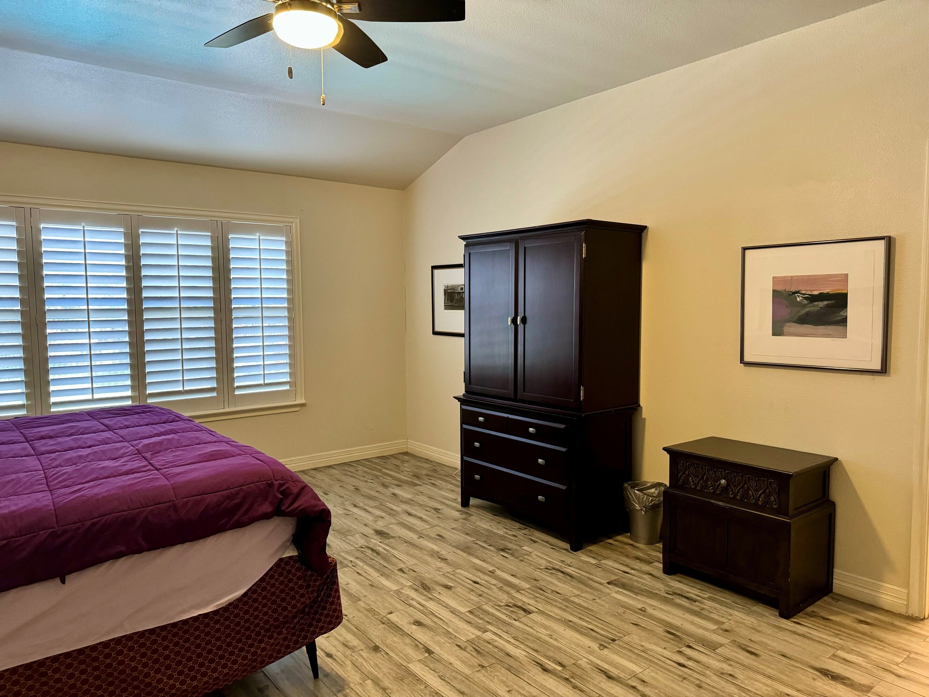 A bedroom with a bed, a wardrobe, a framed picture, and a ceiling fan.