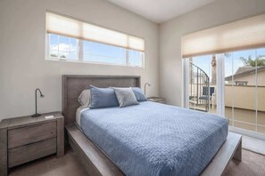 Un dormitorio con cama, mesitas de noche, una ventana con persianas y vistas al exterior.