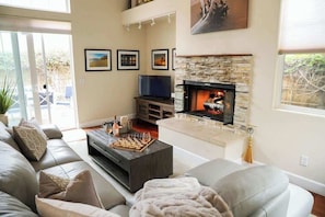 Una sala de estar con chimenea de piedra, un televisor y un tablero de ajedrez sobre una mesa de centro.