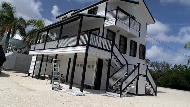 Et toetagers hus ved stranden med balkon, trappe og overdækket veranda.