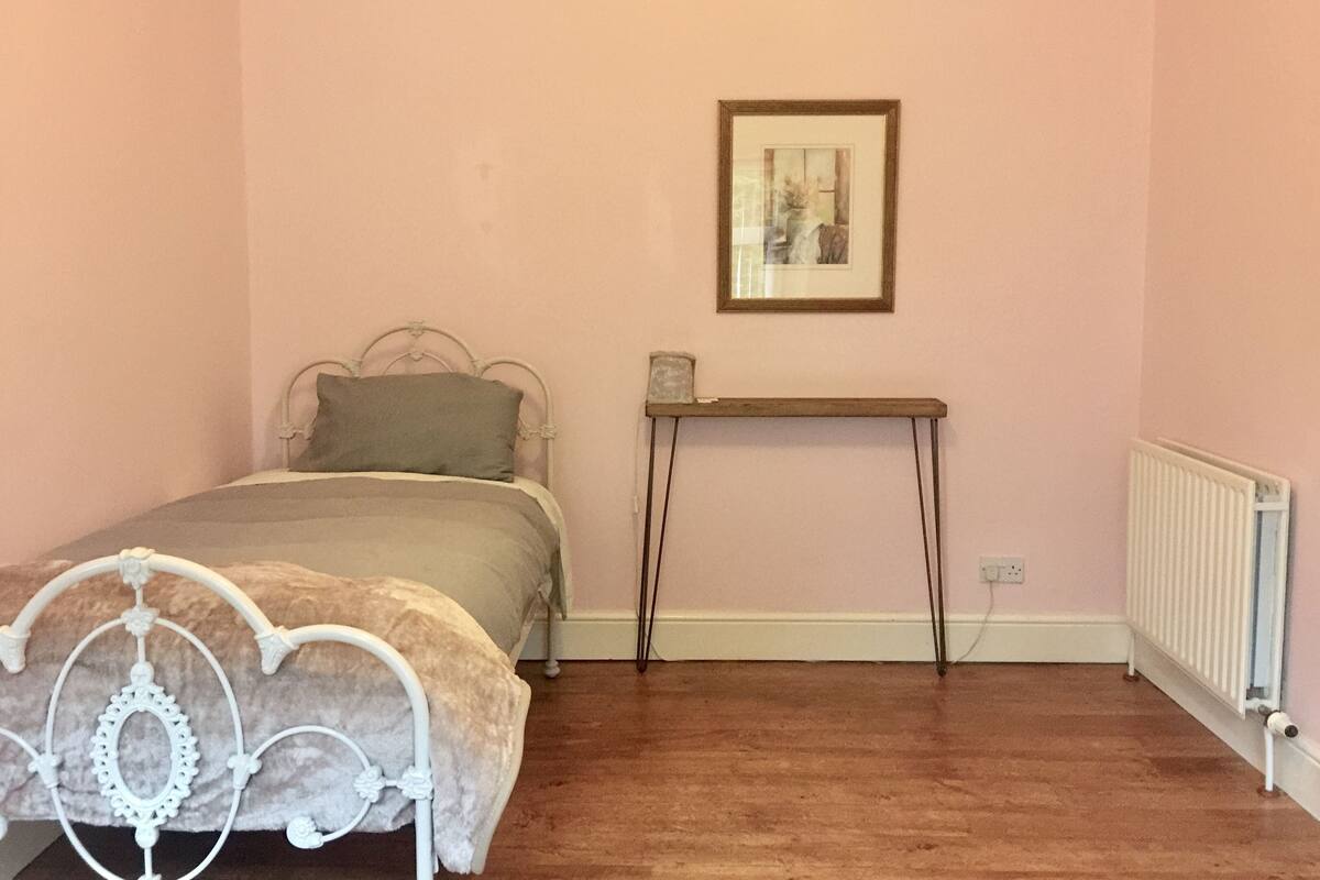 A bedroom with a bed, a bedside table, a framed picture on the wall, and a radiator.