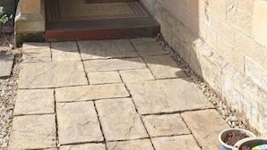 A stone-paved entrance with a green door, hanging flower baskets, and a small step leading to the door. - Glasgow Emo (Glasgow)