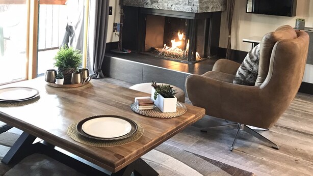 A cozy living room with a fireplace, a comfortable armchair, and a dining table with placemats and a plate.