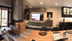 A modern living room with a fireplace, a dining area, and a kitchen with dark cabinetry.