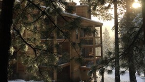 A cabin surrounded by snow-covered trees with a clear view of the sun setting in the background.