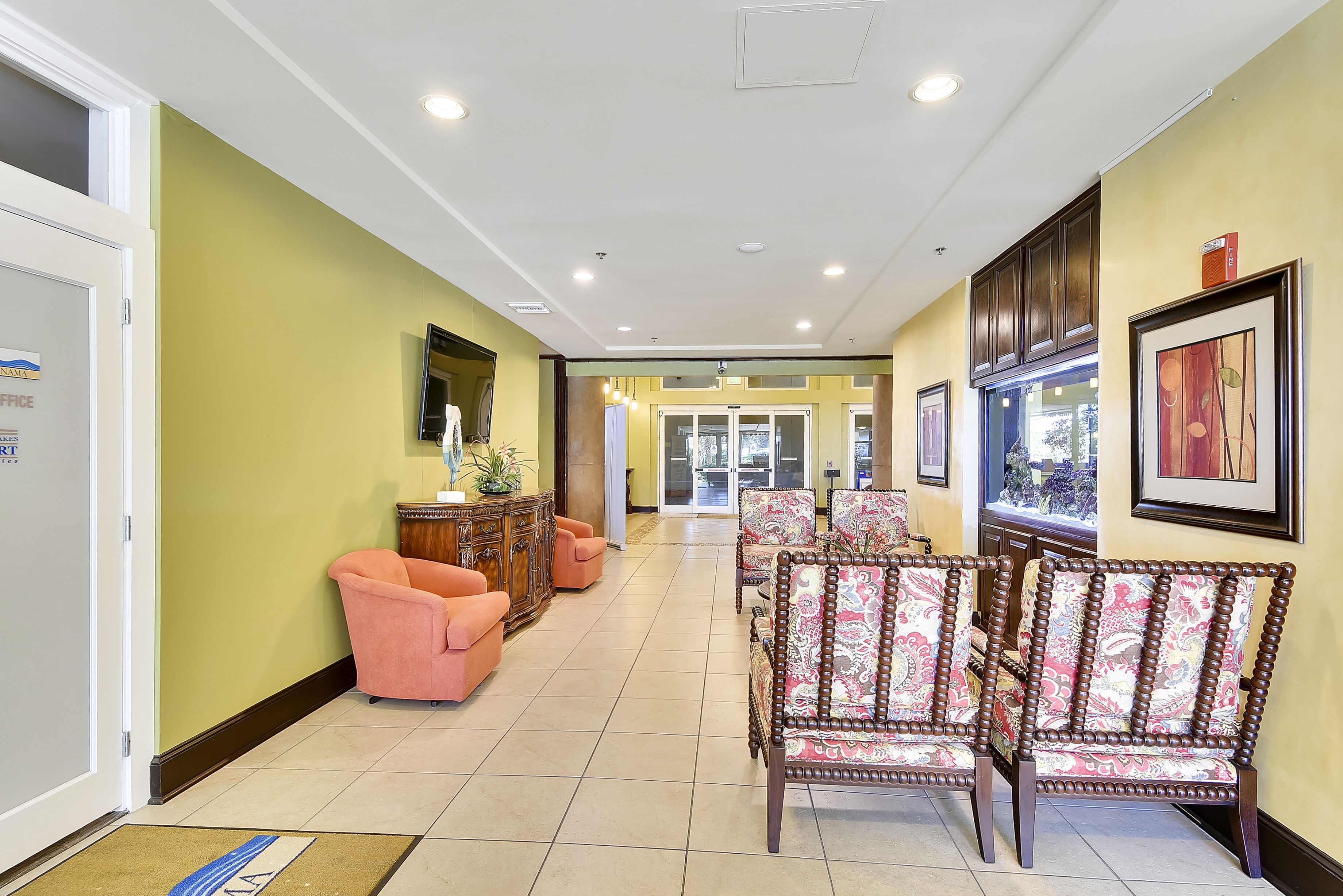 A hotel lobby with a reception desk, a waiting area with chairs, and a large window providing a view of the outdoors.