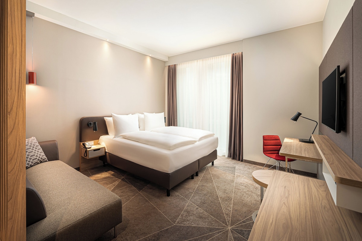 Una habitación de hotel moderna con una cama grande, un escritorio, una silla y un televisor.